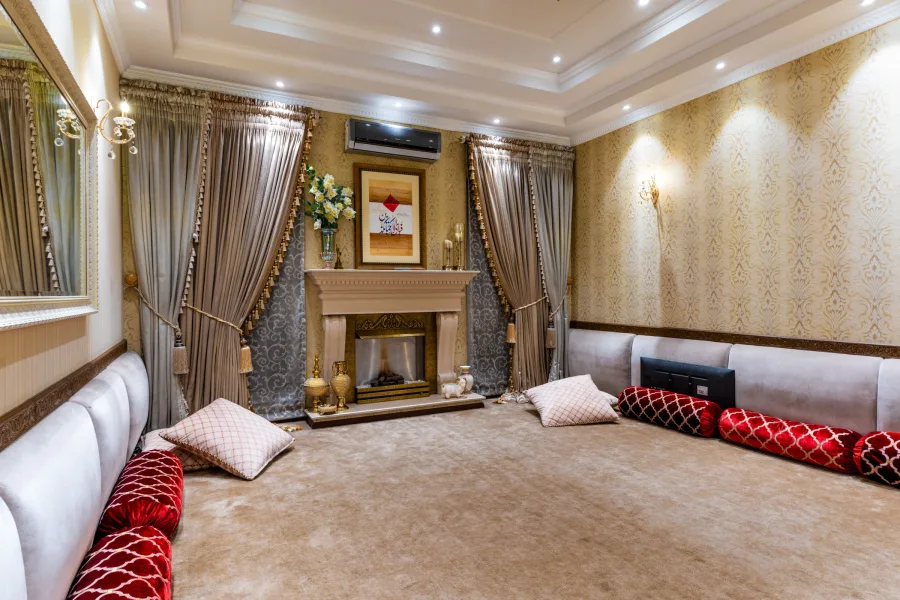 A long majlis with low seating along the walls and full-length curtains held back with tie-backs at the windows