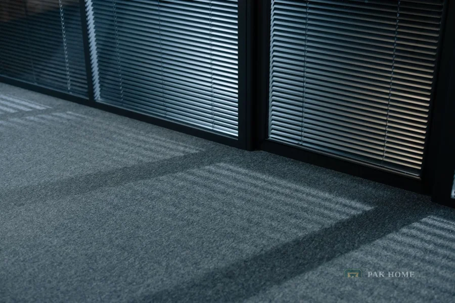 Aluminium venetian blinds along an office window casting lines across a carpeted floor