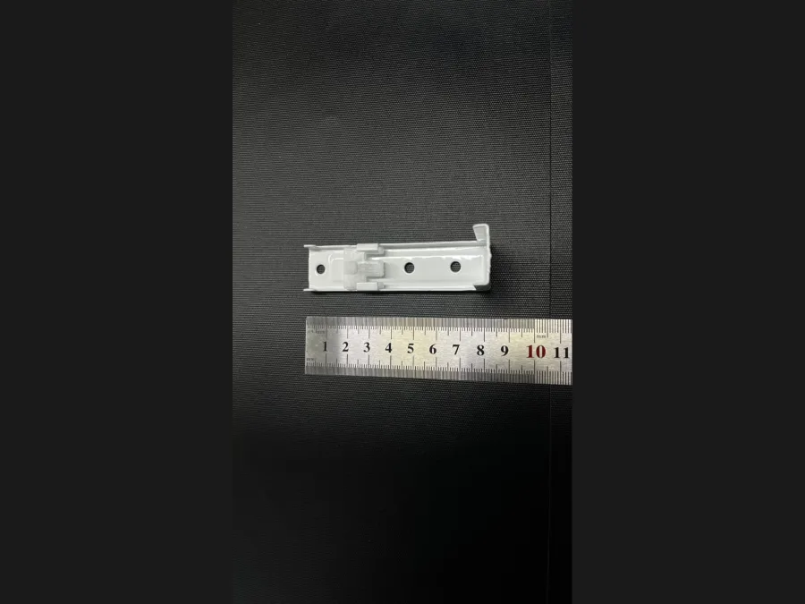 Short white curtain track bracket laid on a ruler