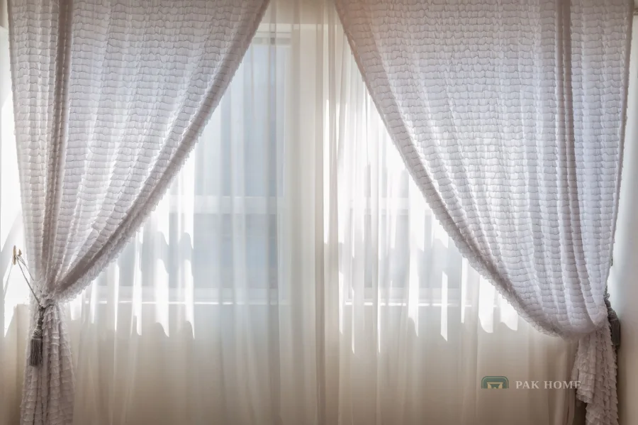 Pair of sheer curtains tied back with tassels at both sides of a bright window