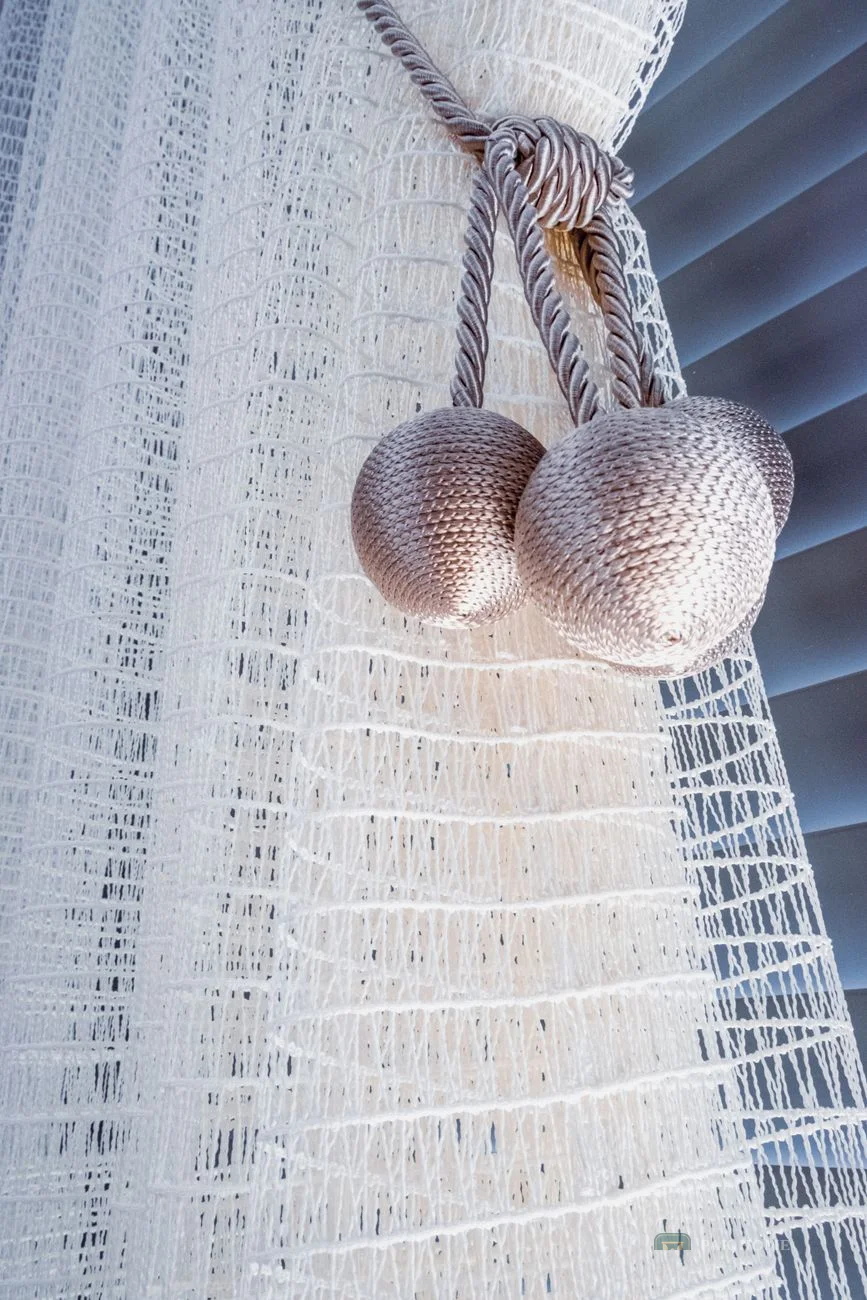 Close-up of tasselled tie-backs holding a pair of white textured curtains